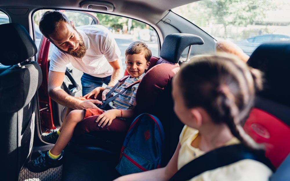 Papa Allaccia la Cintura di Sicurezza al Bambino sul Seggiolino